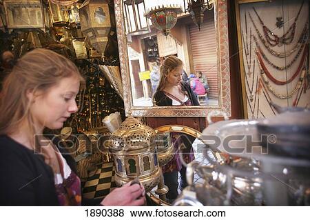 Stock Photo - Young Woman Browsing For Antiques In A Market Stall In The Souk.. Fotosearch