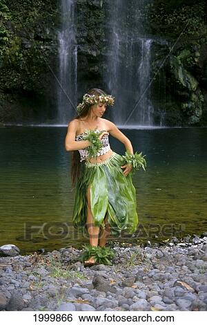 Stock Photograph - Young Woman Hula On Rocks In Front Of Waterfall, Ti Leaf Skirt, Flower Haku. Fotosearch