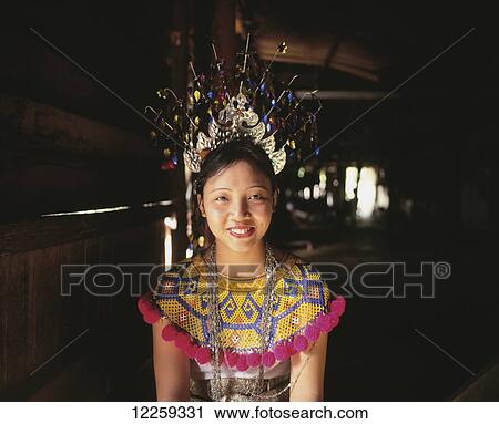 Stock Image - Young woman kneeling in a village long house in traditional dress; Sarawak. Fotosearch