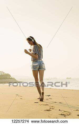 Picture - Young woman listening to music with her headphones on the beach; Xiamen, China. Fotosearch