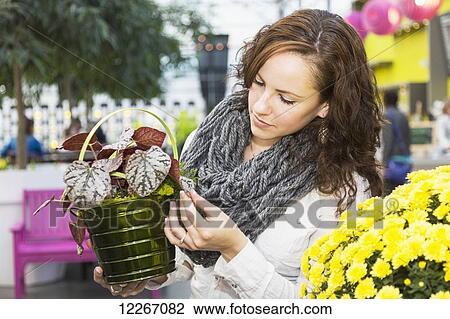 Stock Image - Young woman looking at potted plants in greenhouse store inside mall; St. Albert, Albert, Canada. Fotosearch