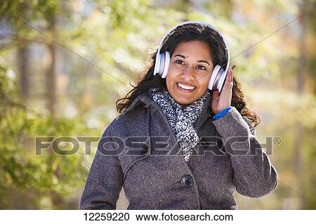 Young woman of South Asian ethnicity listening to music on Bluetooth headphones in Scanlon Creek Conservation Area; Ontario, Canada View Large Photo Image Stock Image - Young woman of South Asian ethnicity listening to music on Bluetooth headphones in Scanlon Creek Conservation Area; Ontario, Canada. Fotosearch