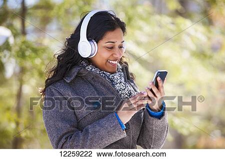 Young woman of South Asian ethnicity using cell phone and Bluetooth headphones in Scanlon Creek Conservation Area; Ontario, Canada View Large Photo Image Stock Image - Young woman of South Asian ethnicity using cell phone and Bluetooth headphones in Scanlon Creek Conservation Area; Ontario, Canada. Fotosearch