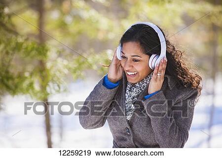 Stock Photo - Young woman of South Asian ethnicity listening to music on Bluetooth headphones in Scanlon Creek Conservation Area; Ontario, Canada. Fotosearch