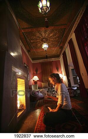 Stock Photo - Young Woman Reading Book By Fireplace In Riad, Marrakech, Morocco. Fotosearch