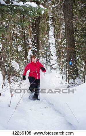 Stock Photo - Young woman runs in her snowshoes through a snow covered forest in winter; Ontario, Canada. Fotosearch