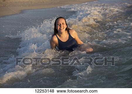 Stock Photo - Young woman sitting in the waves by the beach; Nokomis, Florida, United States of America. Fotosearch