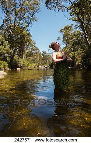 Stock Image - Young woman standing in a creek doing yoga poses; Threadbo, New South Wales, Australia. Fotosearch