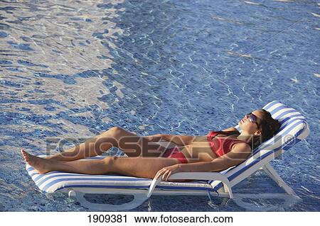 Stock Image - Young Woman Sunbathing On Sunlounger By Swimming Pool On Mayan Riviera, Yucatan Peninsular, Quintana Roo State, Mexico. Fotosearch