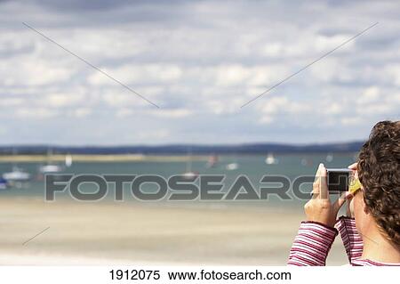 Stock Photography - Young Woman Taking Photo On Beach With Digital Camera, Chichester Harbour, England, Uk. Fotosearch