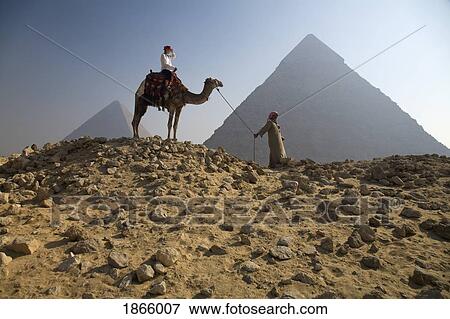 Stock Photo - Young Woman Tourist On A Camel Led By A Guide At The Pyramids Of Giza, Egypt. Fotosearch