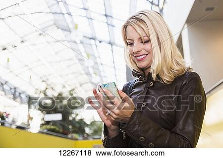 Stock Photo - Young woman using smart phone in shopping complex; St. Albert, Alberta, Canada. Fotosearch