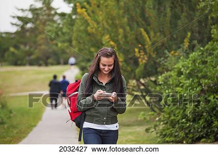 Stock Photo - Young Woman Walking On A Path In A Park Checking Text Messages; Edmonton Alberta Canada. Fotosearch