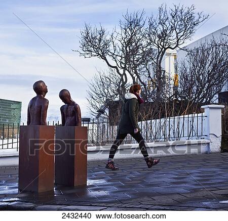 Stock Image - Young woman walking on a walkway with Harpa Concert Hall in background; Reykjavik, Iceland. Fotosearch