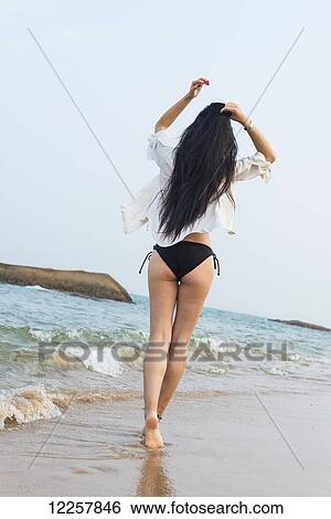Stock Photograph - Young woman walking on the beach in a bikini; Xiamen, China. Fotosearch