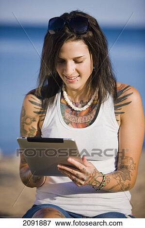 Stock Photo - Young Woman With Tattoos Using A Tablet While Sitting By Lake Simcoe; Ontario Canada. Fotosearch