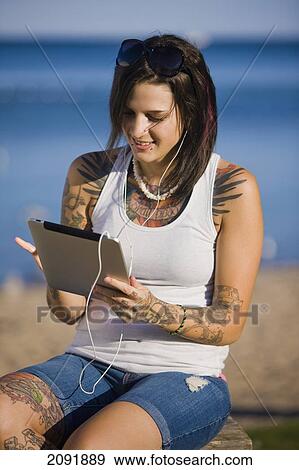 Young Woman With Tattoos Using A Tablet And Ear Buds By Lake Simcoe; Ontario Canada View Large Photo Image Stock Photo - Young Woman With Tattoos Using A Tablet And Ear Buds By Lake Simcoe; Ontario Canada. Fotosearch