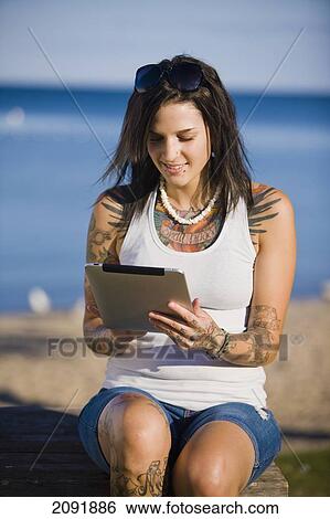 Young Woman With Tattoos Using A Tablet While Sitting By Lake Simcoe; Ontario Canada View Large Photo Image Stock Photograph - Young Woman With Tattoos Using A Tablet While Sitting By Lake Simcoe; Ontario Canada. Fotosearch
