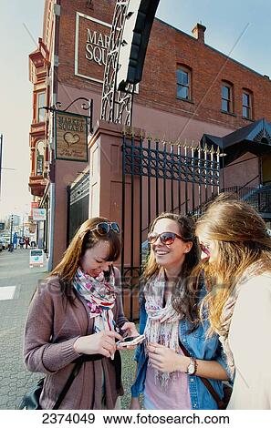 Young Women Checking Phone Directions By Market Square On Lower Johnson Street; Victoria, Vancouver Island, British Columbia, Canada View Large Photo Image Stock Photo - Young Women Checking Phone Directions By Market Square On Lower Johnson Street; Victoria, Vancouver Island, British Columbia, Canada. Fotosearch
