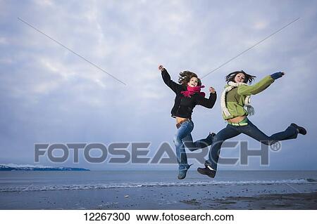 Stock Image - Young women playing and jumping on the Homer Spit, Kenai Peninsula, Southcentral Alaska. Fotosearch