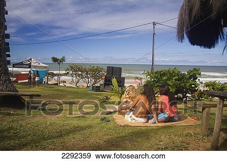 Stock Photo - Young women sitting on grass next to beach; Itacare, Bahia State, Brazil. Fotosearch