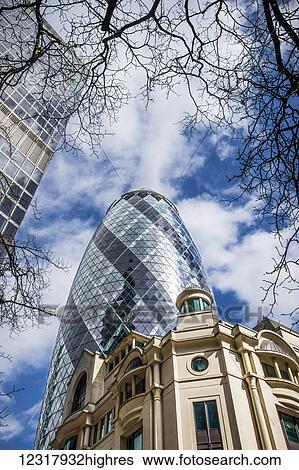 Stock Photograph - 30 St Mary Axe and BPP University framed by tree branches against a blue and clouded sky; London, England. Fotosearch