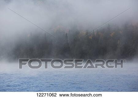 Stock Image - A canoe glides through the morning mist on Rock Lake in Algonquin Provincial Park; Ontario, Canada. Fotosearch
