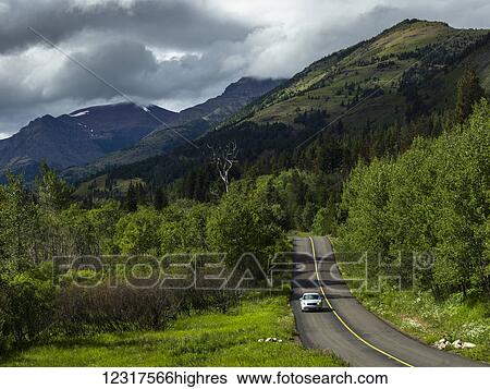 Stock Photograph - A car drives along the road in Waterton Lakes National Park; Alberta, Canada. Fotosearch