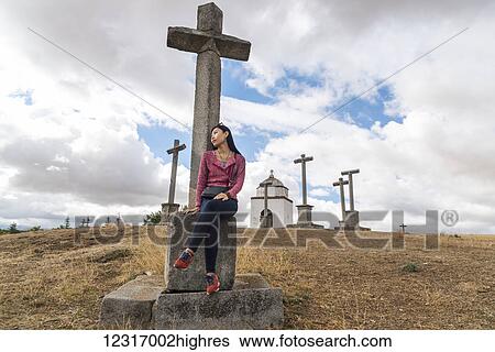 Stock Photograph - A Chinese young woman sitting on a cross in the surroundings of Segovia; Segovia, Castilla Leon, Spain. Fotosearch