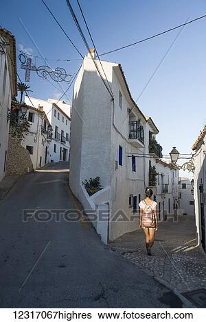 Stock Photograph - A Chinese young woman walking on the street of the beautiful town of Altea in Costa Blanca; Altea, Alicante, Spain. Fotosearch