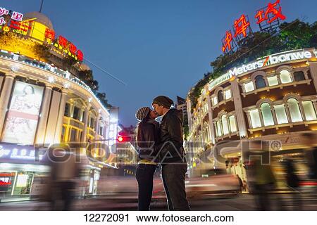 Stock Image - A couple kissing with the blur of traffic and pedestrians in the background; Hong Kong, China. Fotosearch