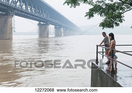 A couple stands at the water's edge of the Yangtze River with a view of the Wuhan bridge at sunset; Wuhan, Hubei province, China View Large Photo Image Stock Photo - A couple stands at the water's edge of the Yangtze River with a view of the Wuhan bridge at sunset; Wuhan, Hubei province, China. Fotosearch