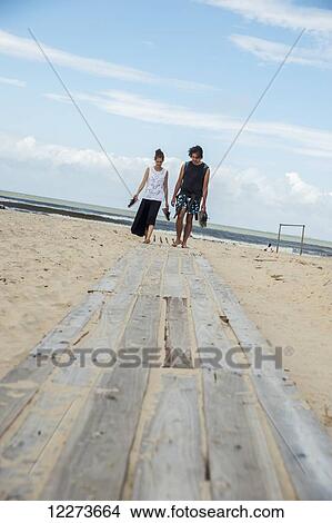 A couple walking barefoot along a wooden boardwalk on the beach, Paseo de las Lindas; Valizas, Uruguay View Large Photo Image Picture - A couple walking barefoot along a wooden boardwalk on the beach, Paseo de las Lindas; Valizas, Uruguay. Fotosearch