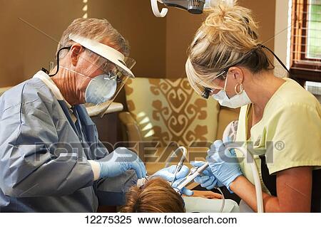 Stock Photography - A dentist and his assistant wearing protective gear and doing a dental proceedure on a patient; United States of America. Fotosearch