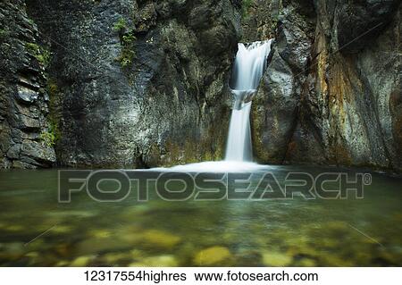 Stock Photograph - A double waterfall drops into green water in a dark canyon, Kananaskis Country; Alberta, Canada. Fotosearch