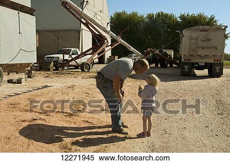 Stock Photography - A farmer and his young daughter share a moment together during his work day of harvesting and storing grain corn, near Sioux City; Iowa, United States of America. Fotosearch