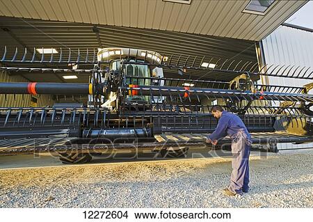 Picture - A farmer works on the cutting bar of the header to his combine, parked in front of the farm repair shop, near Lorette; Manitoba, Canada . Fotosearch
