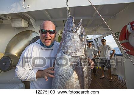 Stock Image - A fisherman poses with a dogtooth tuna (Gymnosarda unicolor); Tahiti. Fotosearch