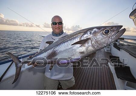 Stock Photograph - A fisherman poses with a dogtooth tuna (Gymnosarda unicolor); Tahiti. Fotosearch