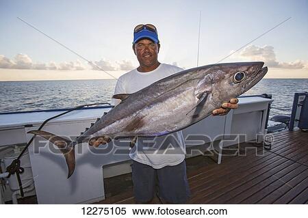 Stock Photography - A fisherman poses with a dogtooth tuna (Gymnosarda unicolor); Tahiti. Fotosearch
