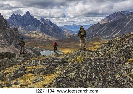 Picture - A group of hikers standing on rocks overlooking the colourful valleys in Tombstone Territorial Park in autumn; Yukon, Canada. Fotosearch