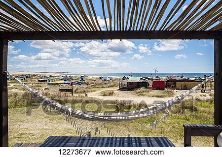 Stock Photo - A hammock hangs under a shaded porch with buildings along the coast; Cabo Polonio, Uruguay. Fotosearch