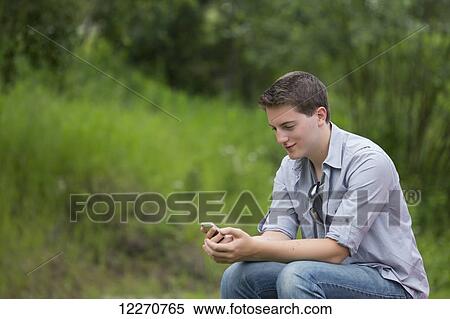 Stock Photography - A high school teenage boy texting on a cell phone on a summer afternoon in Wasilla, Southcentral Alaska.. Fotosearch