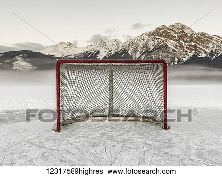 Stock Photograph - A hockey net on frozen Pyramid lake with the rugged Canadian Rockies mountain range in the background, Jasper National Park; Alberta, Canada. Fotosearch