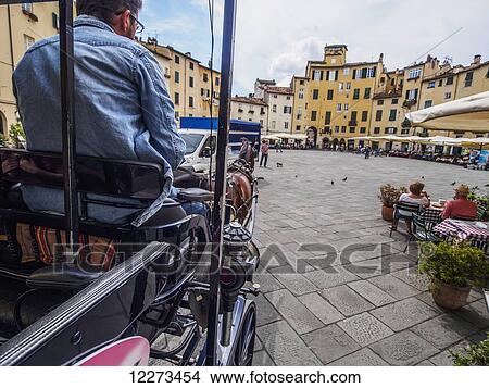 Picture - A horse-drawn carriage makes its way into Piazza dell'Anfiteatro, a piazza in the walled city of Lucca that was once an amphitheatre during the Roman rule; Lucca, Italy. Fotosearch