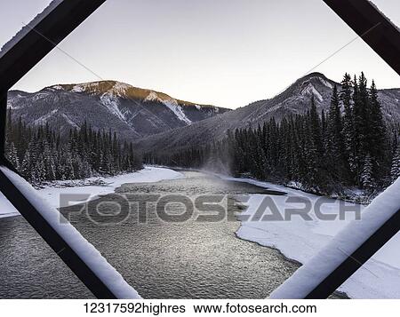 A landscape with snow along the shoreline of a lake and a mountain range viewed through a diamond shaped window frame; British Columbia, Canada View Large Photo Image Stock Photograph - A landscape with snow along the shoreline of a lake and a mountain range viewed through a diamond shaped window frame; British Columbia, Canada. Fotosearch