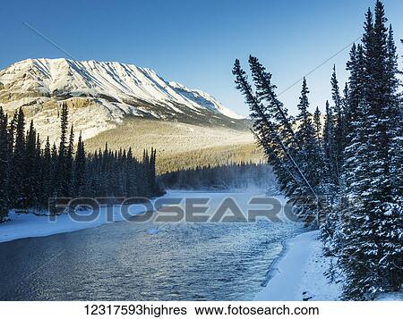 Stock Photograph - A landscape with snow along the shoreline of a lake and a snow covered mountain; British Columbia, Canada. Fotosearch