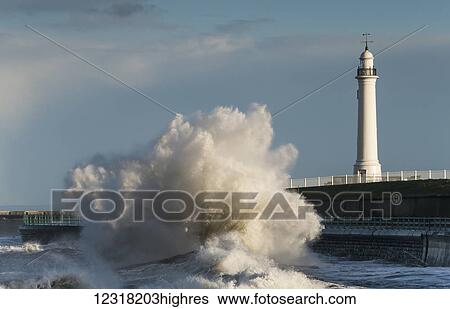 A large wave breaks and crashes against the shore in front of a lighthouse; Sunderland, Tyne and Wear, England View Large Photo Image Stock Photograph - A large wave breaks and crashes against the shore in front of a lighthouse; Sunderland, Tyne and Wear, England. Fotosearch