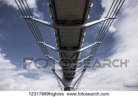 Stock Photograph - A low angle view underneath the Millennium Bridge from the River Thames bank in Bankside; London, England. Fotosearch