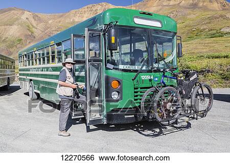 Stock Photograph - A male tourist with a camera enters a park camper bus at Eielson Visitor Center in Denali National Park, Interior Alaska, Summer, USA.. Fotosearch